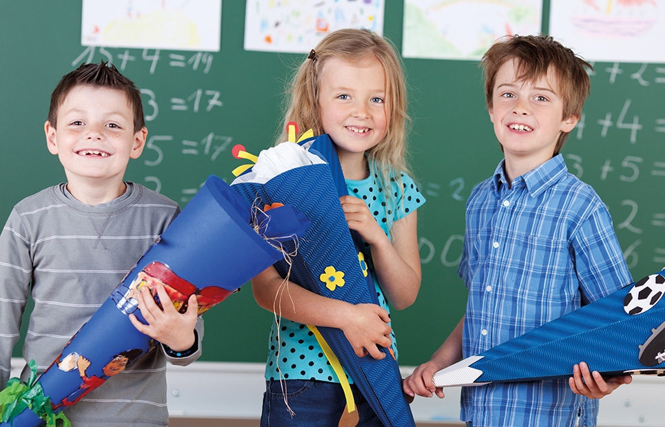 Drei Kinder mit Schultüte in einem Klassenzimmer vor einer Tafel