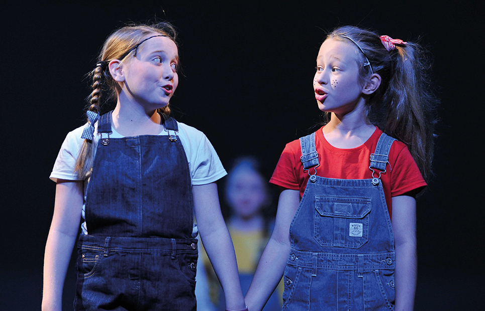Zwei Mädchen die sich an den Händen festhalten und auf einer Bühne stehen und gemeinsam singen