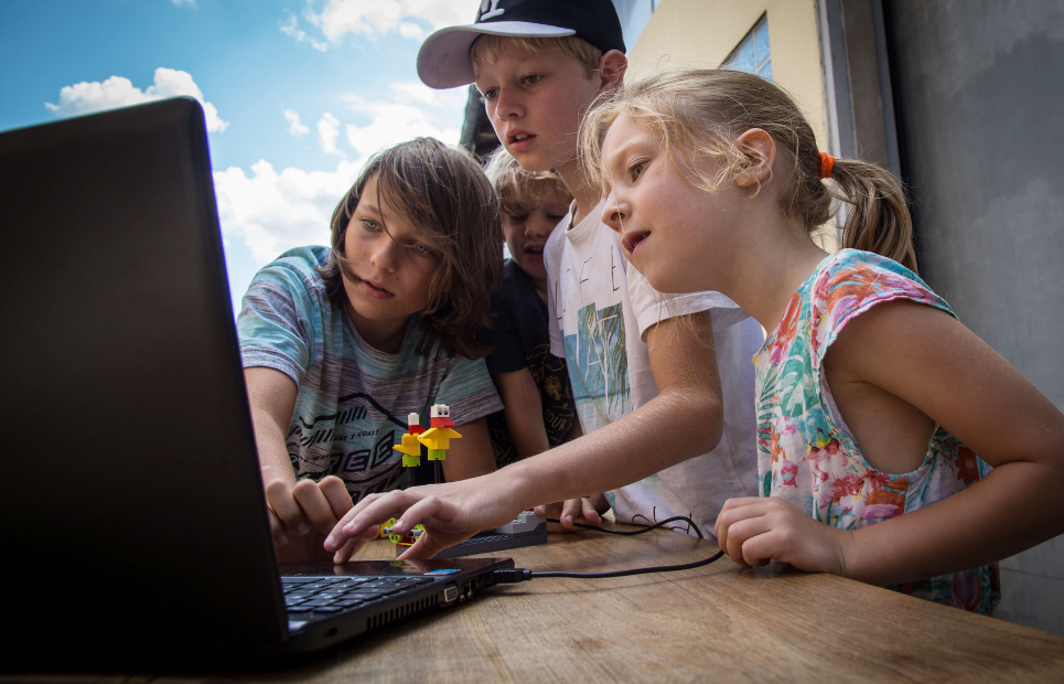 Vier Kinder stehen um einen Laptop zusammen herum und schauen auf den Bildschirm