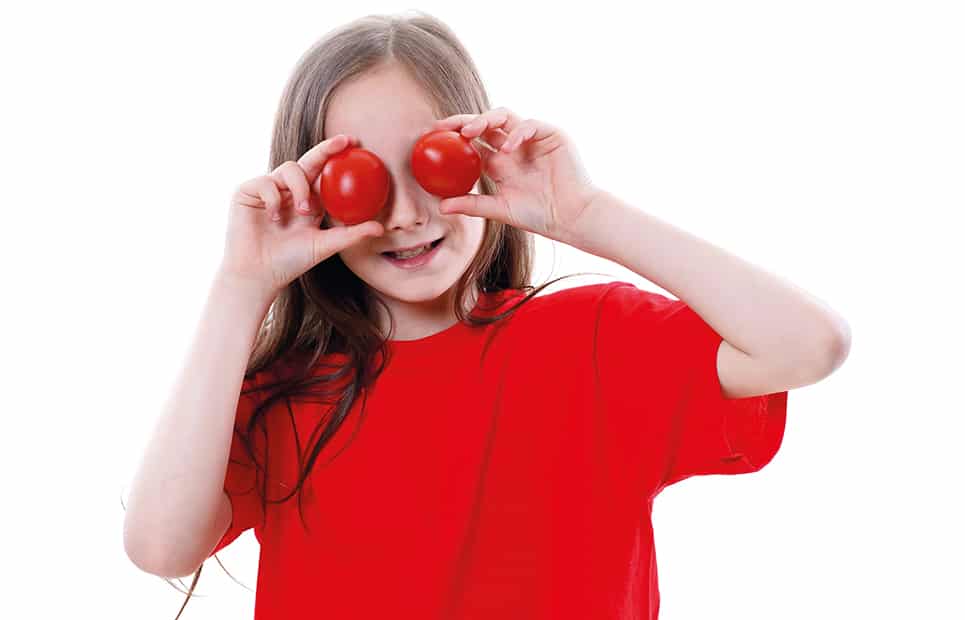 Ein Mädchen in einem roten T-Shirt hält sich zwei Tomaten vor die Augen