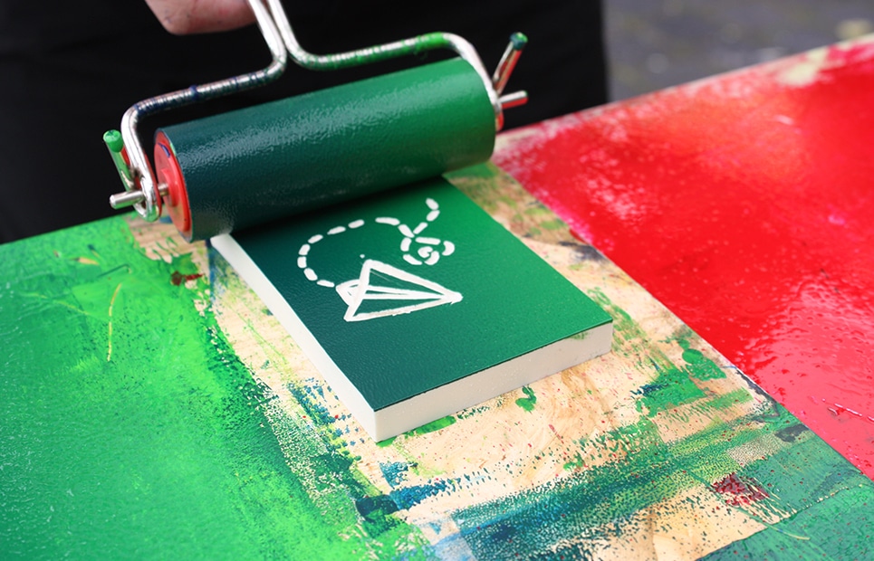 Eine Farbrolle wird mit grüner Farbe über eine Druckplatte mit einem Flugdrachen gerollt