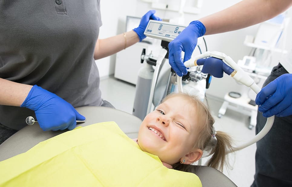 Ein Mädchen liegt auf einem Zahnarztstuhl und zwinkert in die Kamera