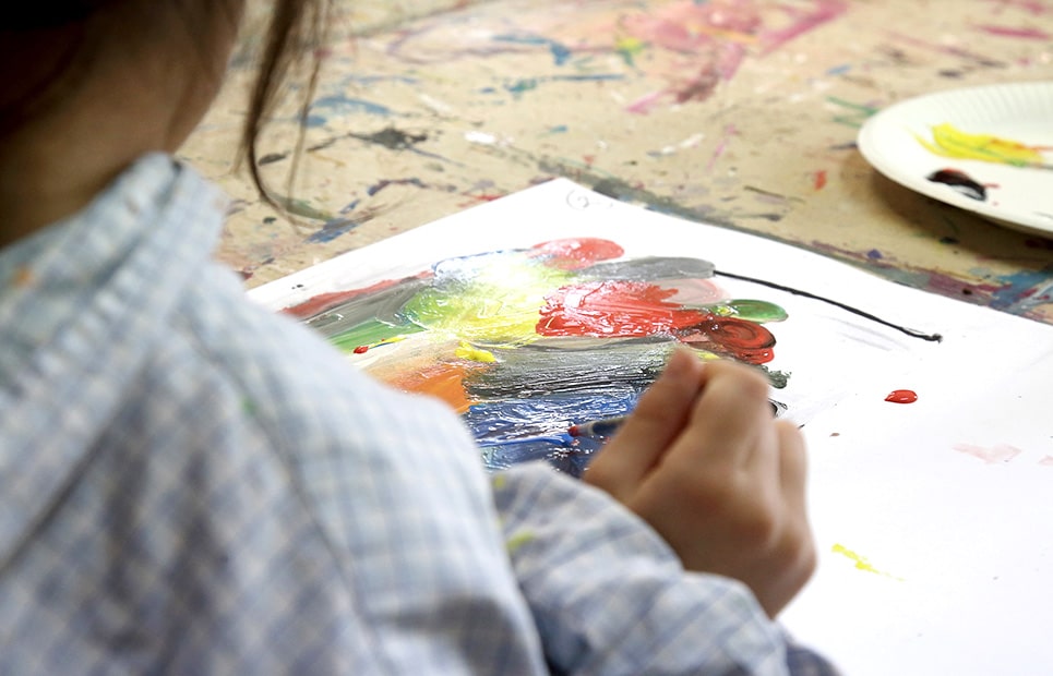Ein Mädchen malt mit einem Pinsel ein buntes Bild