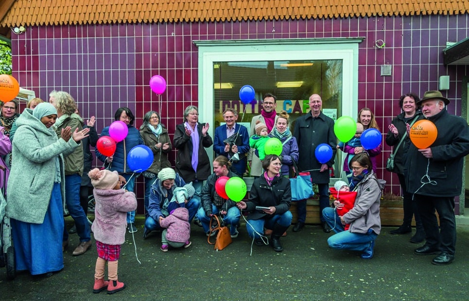 Man sieht eine Gruppe von Eltern mit Kindern mit Luftballons in der Hand vor dem Familienzentrum